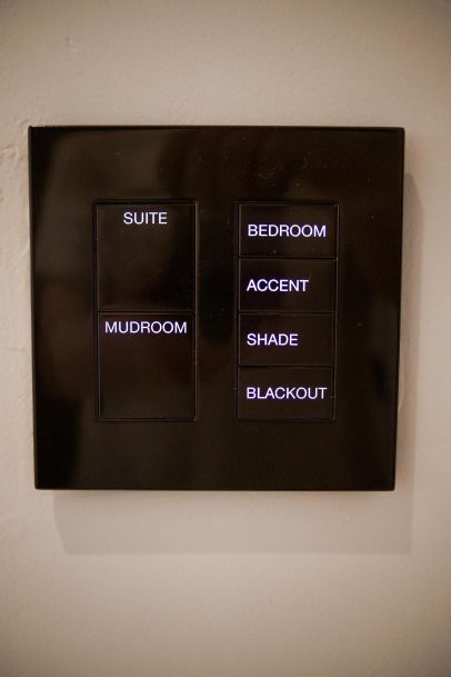 A black smart home control panel with buttons labeled for various areas including Suite, Mudroom, Bedroom, Accent, Shade, and Blackout.