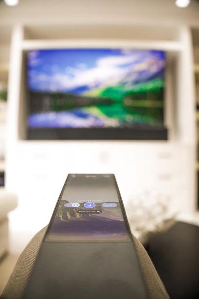 Close-up of a remote control focusing on the TV in the background. The TV displays a vibrant nature scene, and the remote control is used to manage the room's audio-visual system.