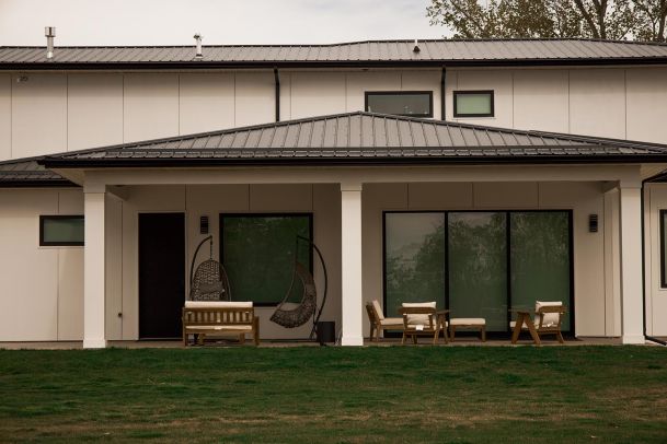 Front view of a contemporary house featuring a cozy patio with outdoor furniture and swing chairs.