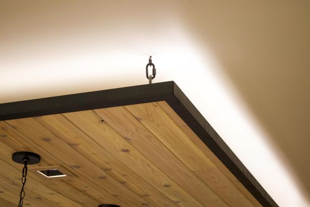 Close-up of a wooden ceiling panel with hanging chains and bright ceiling lighting. 