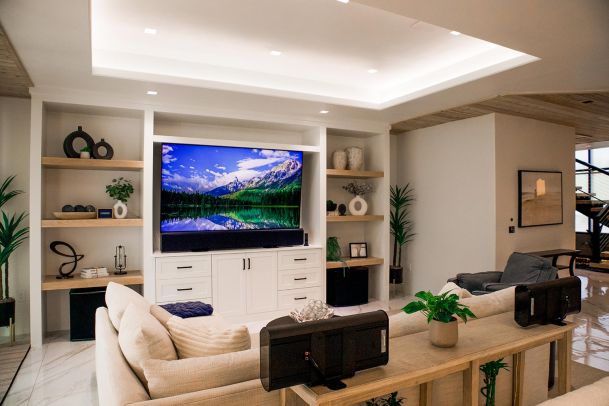 Living room with a large flat-screen TV mounted in a built-in wall unit. The room features a comfortable sofa, decorative shelves, and modern lighting.