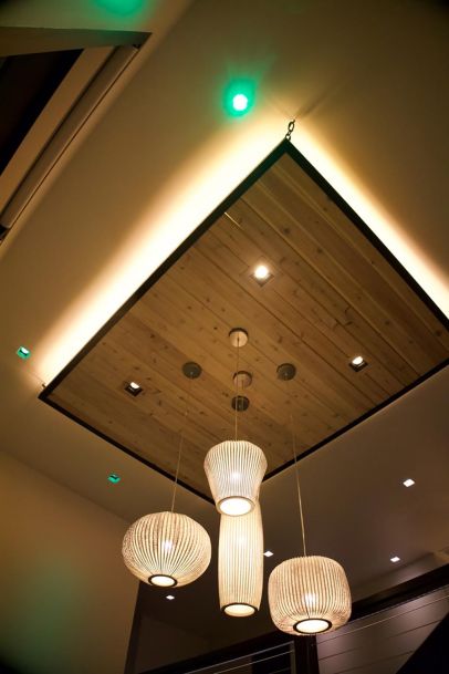 Modern ceiling design featuring a wooden panel insert with hanging pendant lights and green accent lighting. 