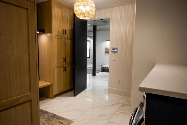 A laundry room with wooden cabinets and a hanging light fixture, leading to a room with open door and visible furnishings.