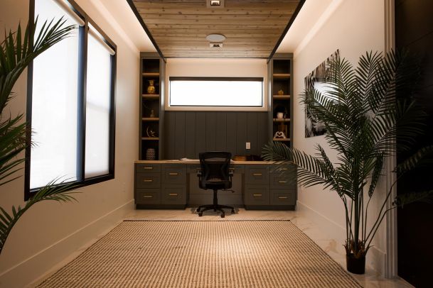 Home office with a central desk, built-in shelving, and large windows.