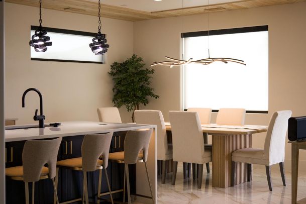 Dining area with a large table, beige chairs, and unique hanging lights. 