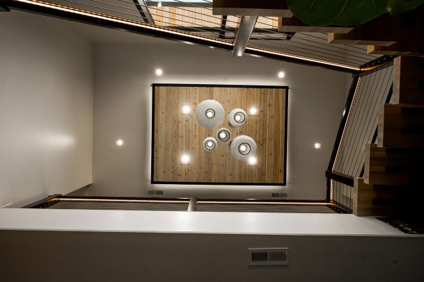 A view from the top of a staircase looking down, showing a modern light fixture with multiple pendant lights hanging over a wooden ceiling with recessed lights around it.