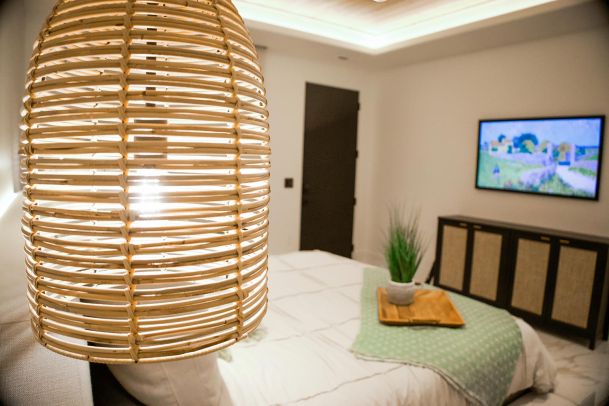 Bedroom featuring a large wicker pendant light, bed with white bedding, and a TV mounted on the wall.