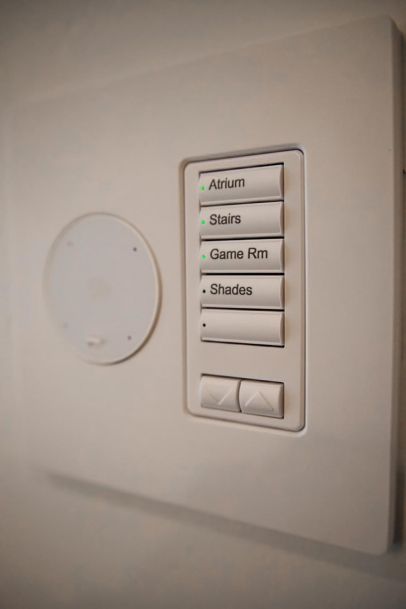 A white Lutron + Josh AI Nano smart home control panel with buttons labeled for various areas including Atrium, Stairs, Game Room, and Shades.