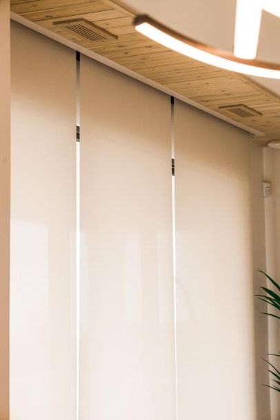 Multiple beige window shades in a row, with a wooden ceiling and a plant visible.