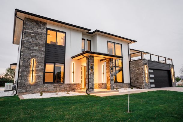 Elegant modern home with stone accents, warm lighting, and a well-maintained lawn.