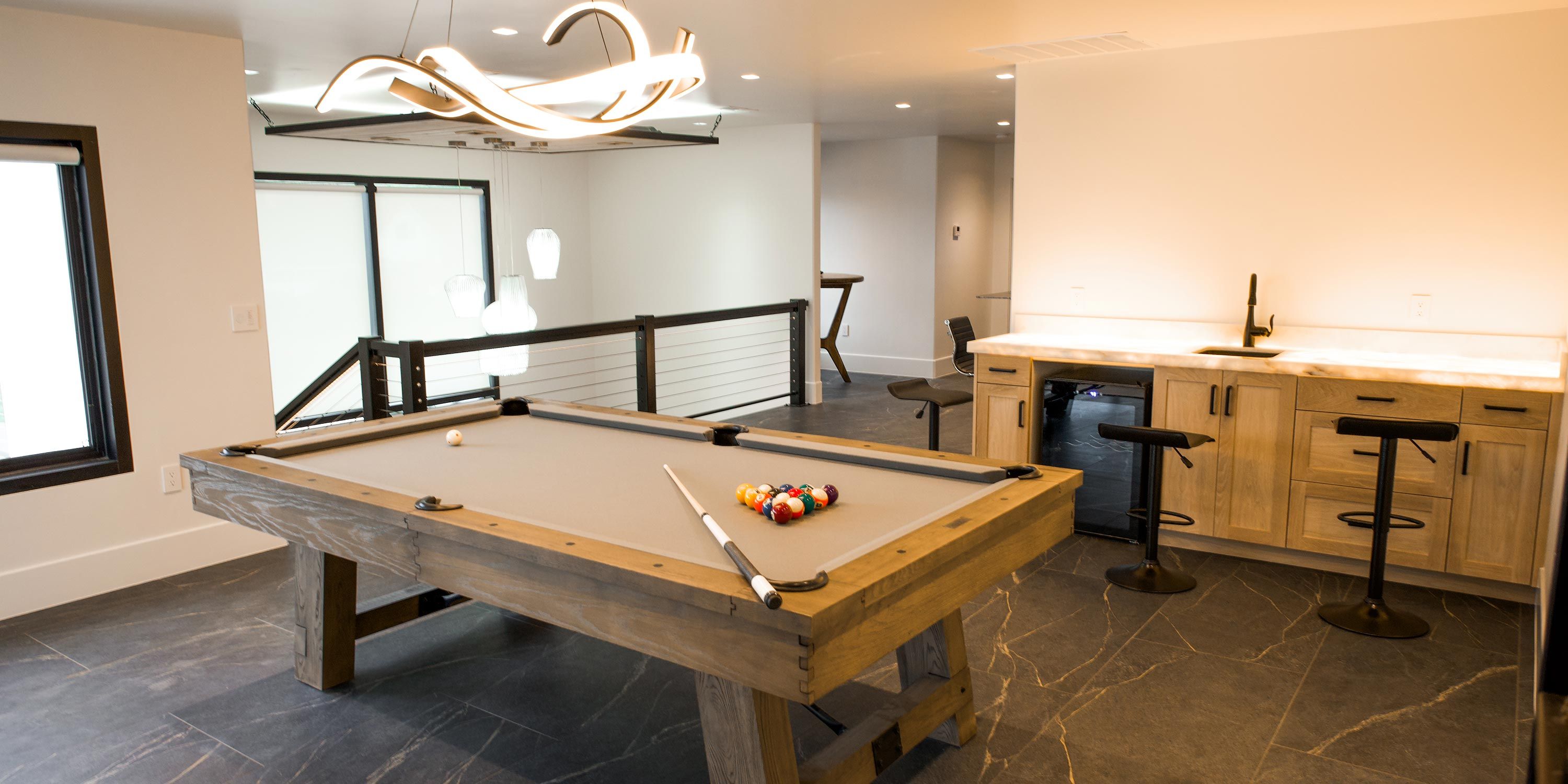 A spacious game room with modern lighting fixtures and a billiards table, featuring Elan home automation controls.