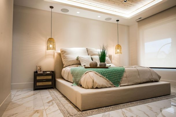 Modern bedroom with a large bed, bedside tables, and hanging pendant lights. The room is illuminated by recessed lighting and features a minimalist design.