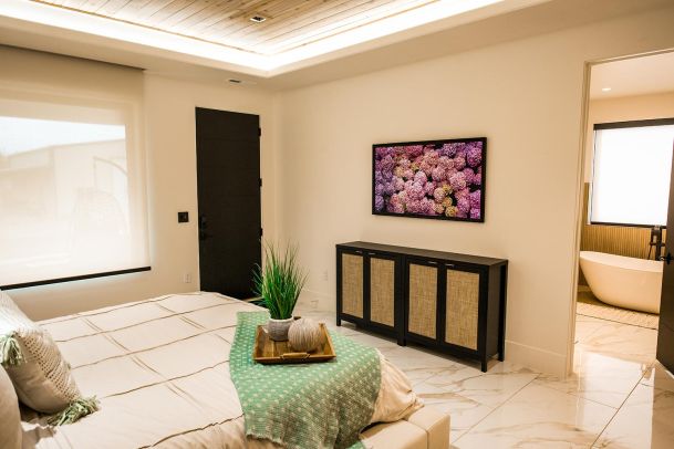 Bedroom with a mounted flat-screen TV displaying a colorful floral image. The room features a modern design with a wooden ceiling and minimalist decor.