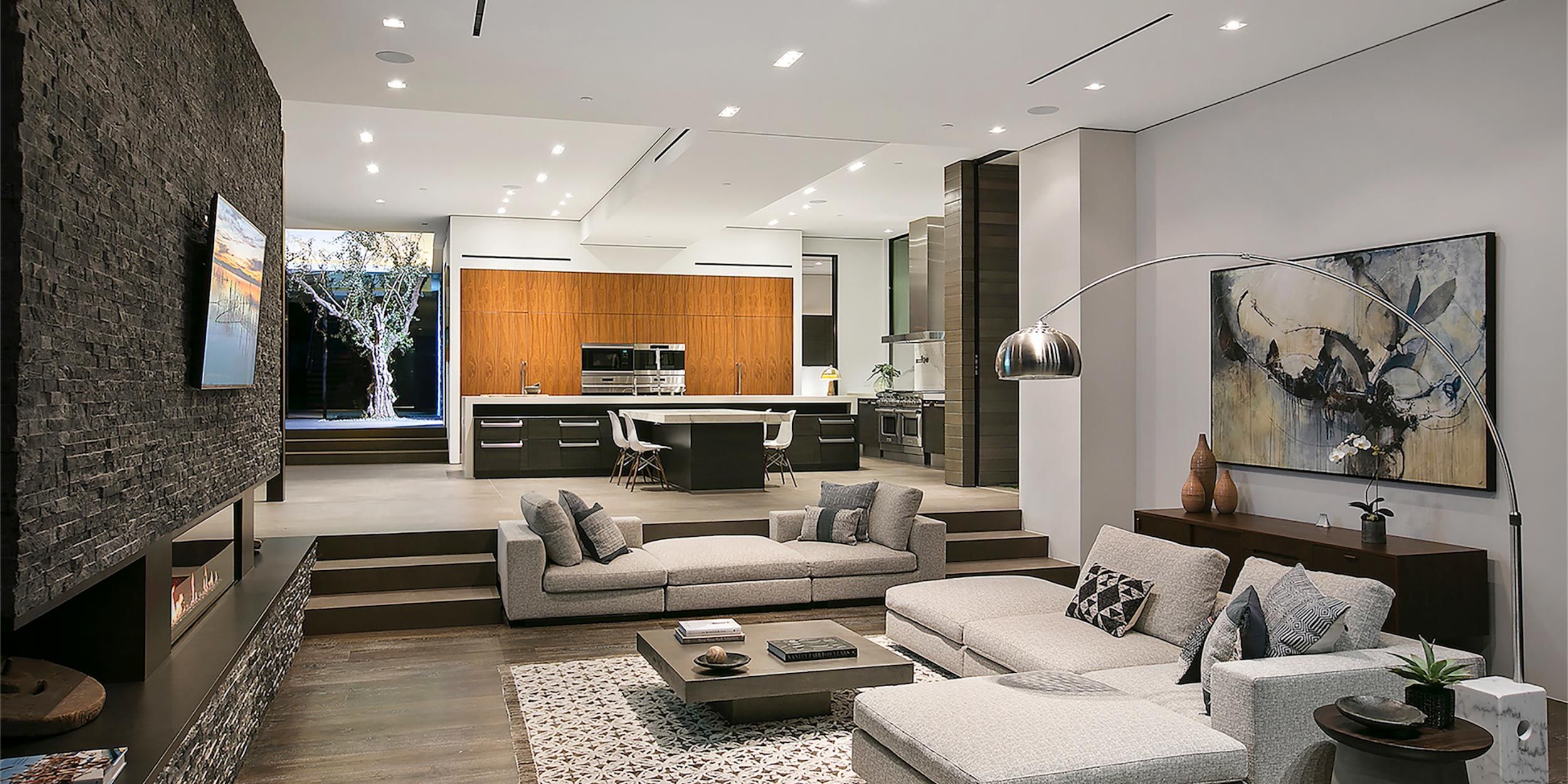 Spacious, modern interior with an open-concept living and dining area, warm lighting, and a scenic outdoor view.