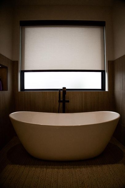 Bathroom with a freestanding bathtub and a large window covered by a light beige shade.