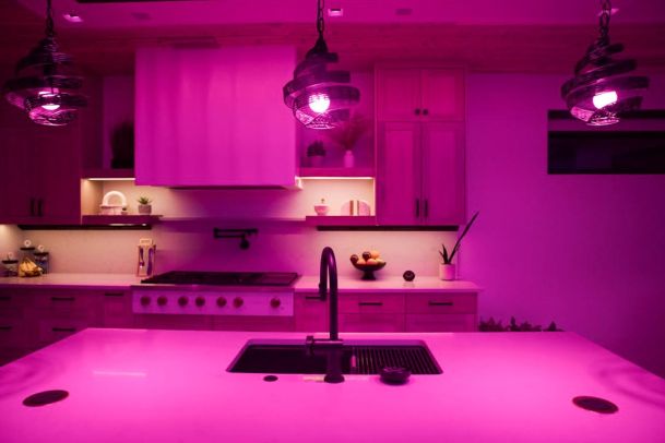 Kitchen with an island, modern appliances, and vibrant pink mood lighting.