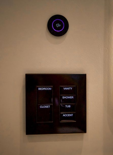 A Lutron smart home control panel with buttons labeled for areas including Bedroom, Vanity, Shower, Tub, Closet, and Accent, with a black Josh AI Nano is above it